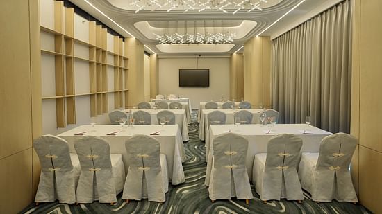 Conference room with white rectangular tables forming a square, surrounded by white chairs. Patterned floor and draped windows - The Orchid Hotel, Chandigarh