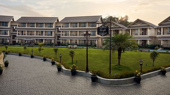 Wide-angle view of a well-maintained lawn surrounded by elegant multi-storey resort buildings at sunset - Voyage The Solitaire Bliss.