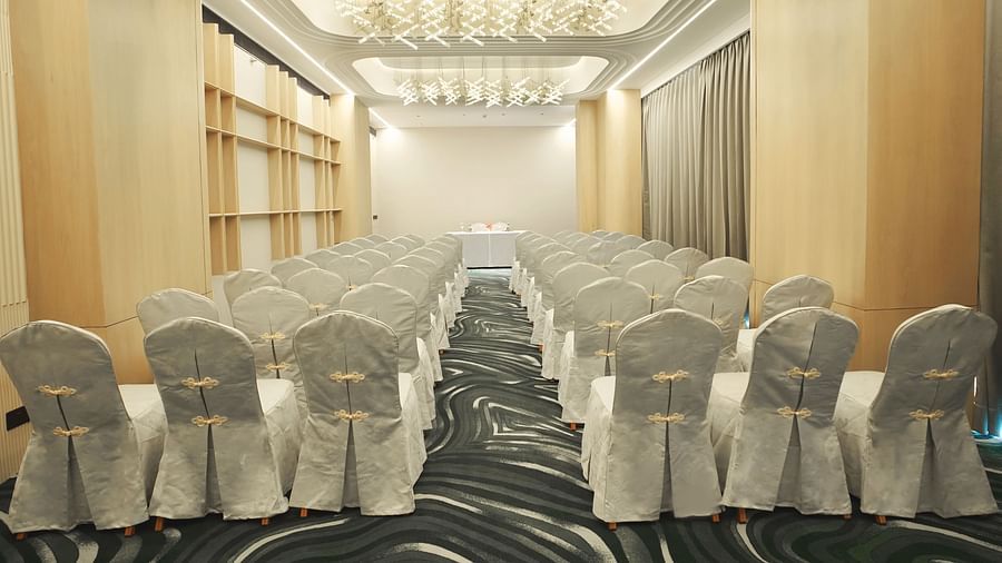 Long view of a conference room with rows of white-covered chairs facing forward. Patterned carpet and modern ceiling lights - The Orchid Hotel, Chandigarh