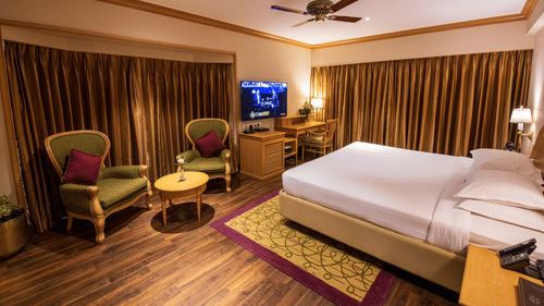 A room with a double bed, wooden furniture seating area with green & brown accents at The Clarton. One of the finest Kodaikanal rooms near lake.