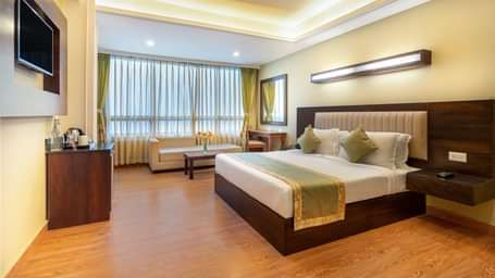 Deluxe Room at Summit North Star, Gangtok featuring a bed, a flat TV screen, a cabinet with tea and coffee maker, a mirror, work desk and chair, and a sofa set with centre table.