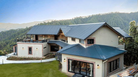 Front elevation with grey pitched metal roofs, brick-trimmed cream walls, lantern lights, sliding glass doors and a lawn with path lights at The Chamomile Estate.