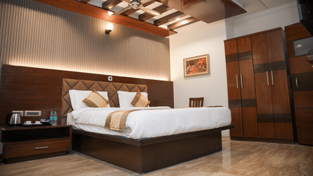 Suite at The OnTime Bangalore featuring a well-lit hotel bedroom with a large bed, golden pillows and runner, and dark wooden furniture.