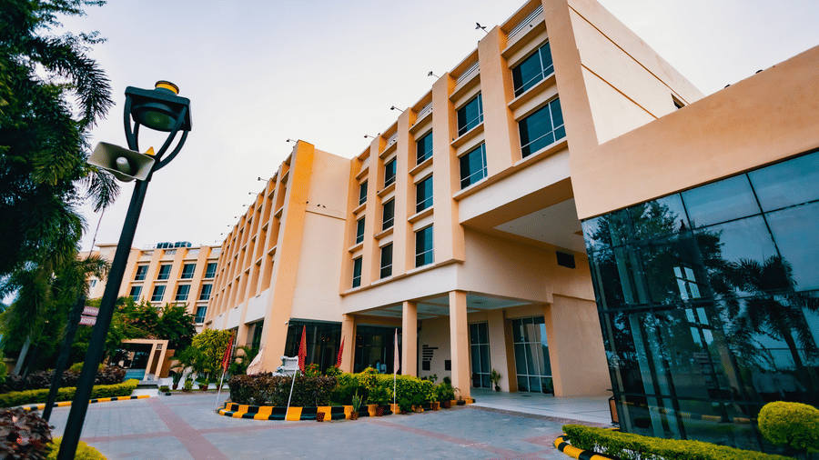 A modern hotel exterior at Ramada by Wyndham Bodh Gaya Mahabodhi, featuring a glass entrance and is seen under clear daylight.