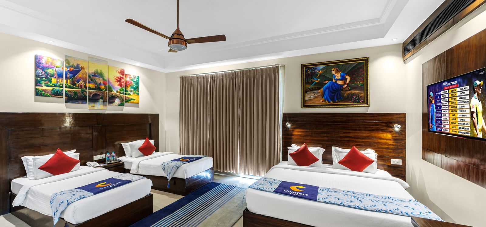 Well furnished huge room with a king size bed and twin beds featuring a ceiling fan, artwork above bedside table, and TV unit opposite the beds at Inder Reva Resorts Rishhikesh.