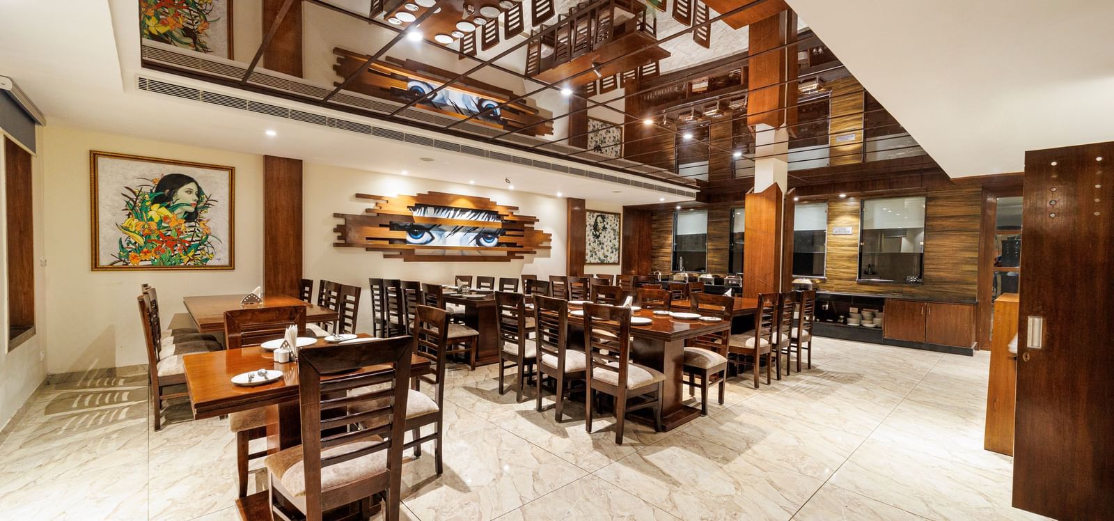 Restaurant at Inde Reva Resorts Rishhikesh featuring wooden furniture, open ceiling design, framed art, and tiled flooring.