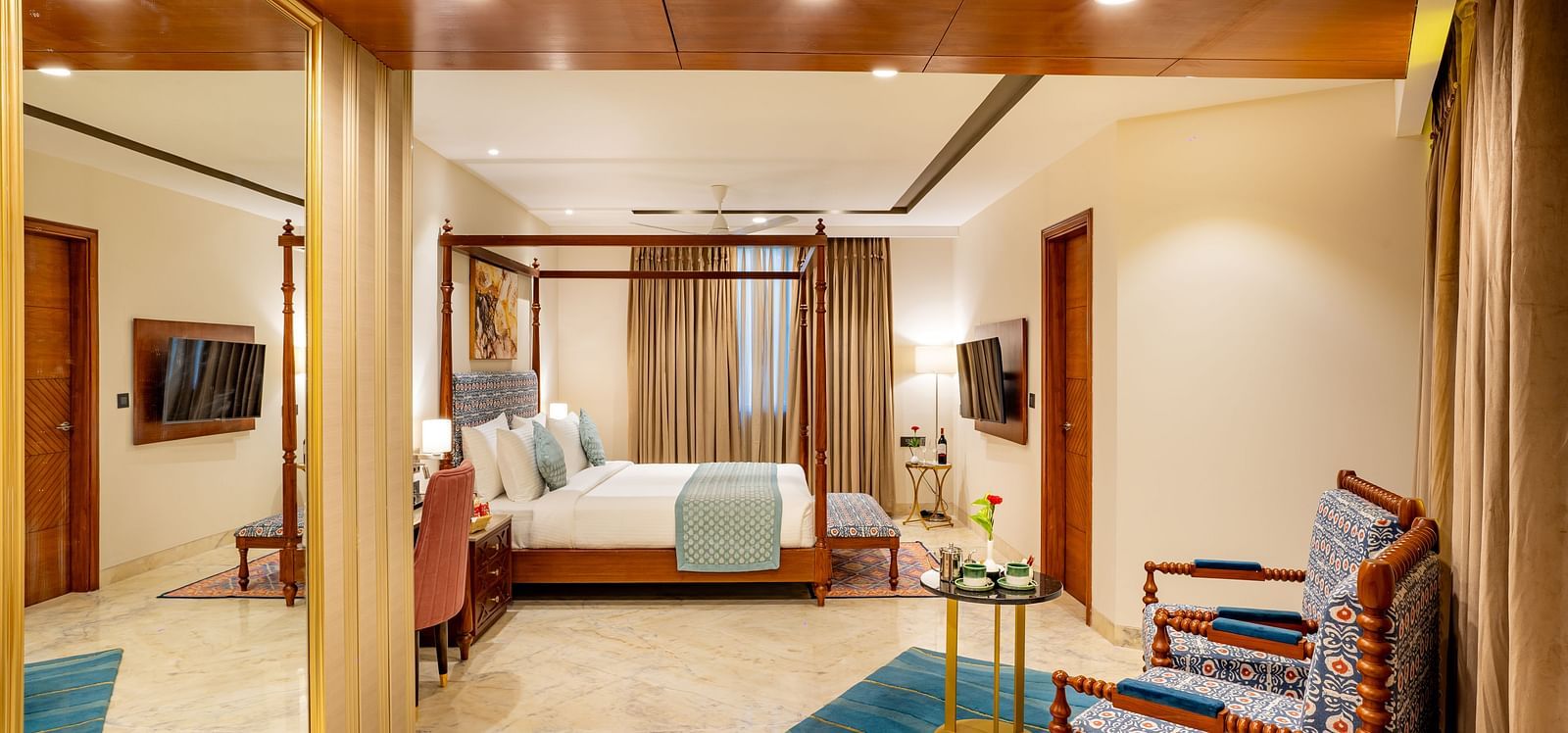 An image of a bedroom with flat TV screen, king size bed, a chair, and one centre table