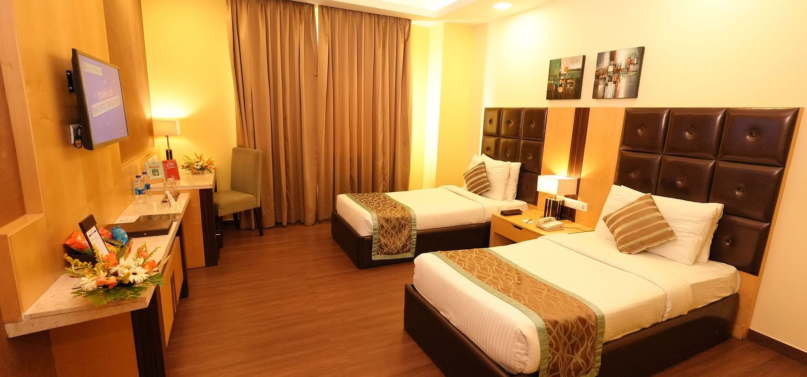 Hotel room with a bed featuring striped bedding and a television on the wall - Grand Plaza Lords Inn Jammu