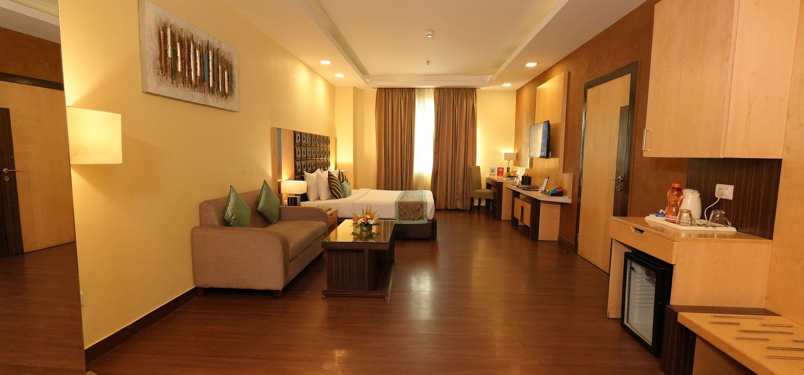 Hotel suite hallway leading to a seating area and a bed with striped bedding - Grand Plaza Lords Inn Jammu