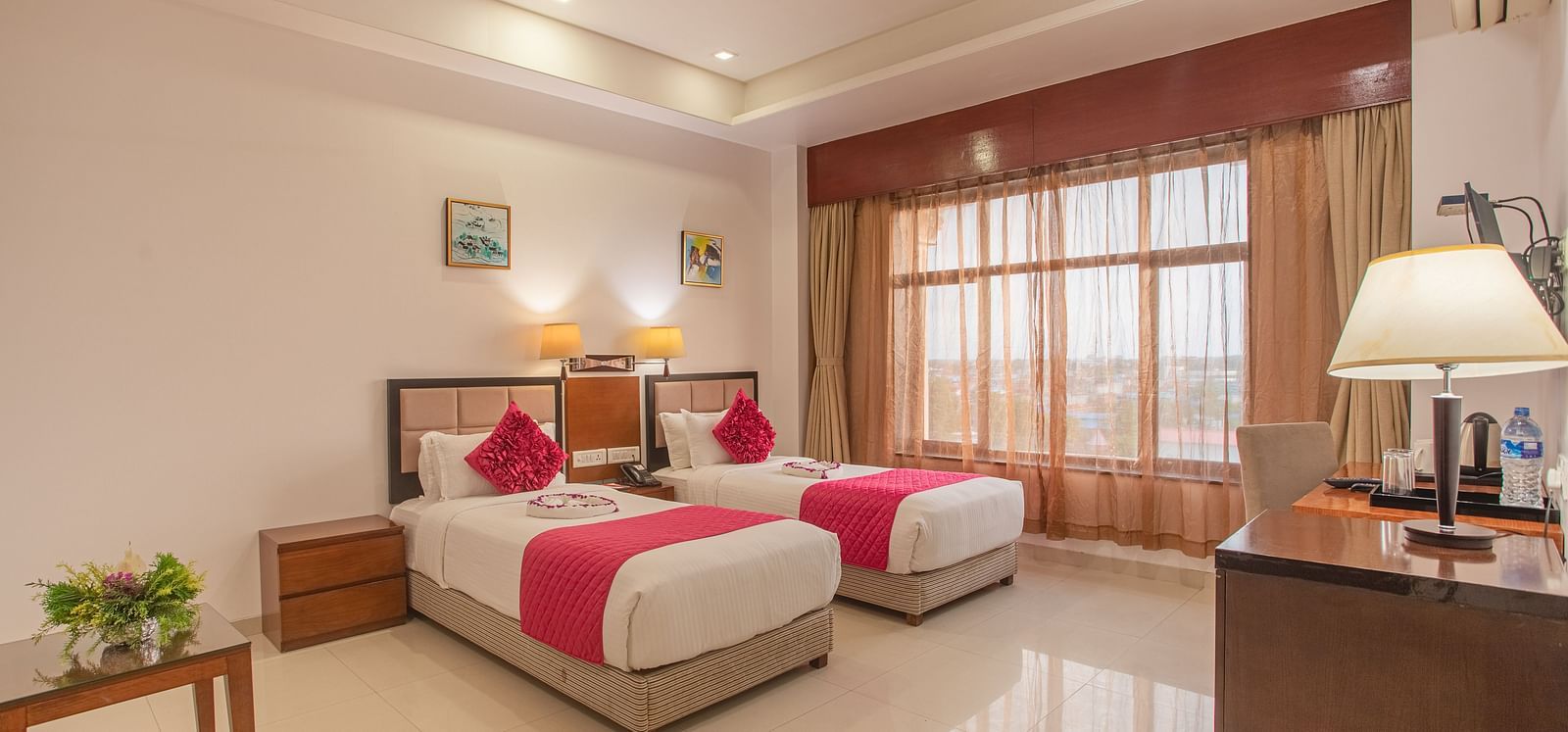 Bright twin room at Diamond Palace Lords Plaza with two single beds featuring pink accents, a work desk, and a small table.