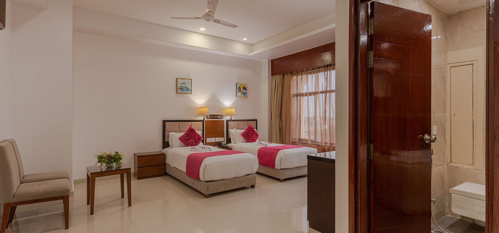 A twin room at Diamond Palace Lords Plaza with two single beds featuring pink accents and a glimpse into the bathroom.
