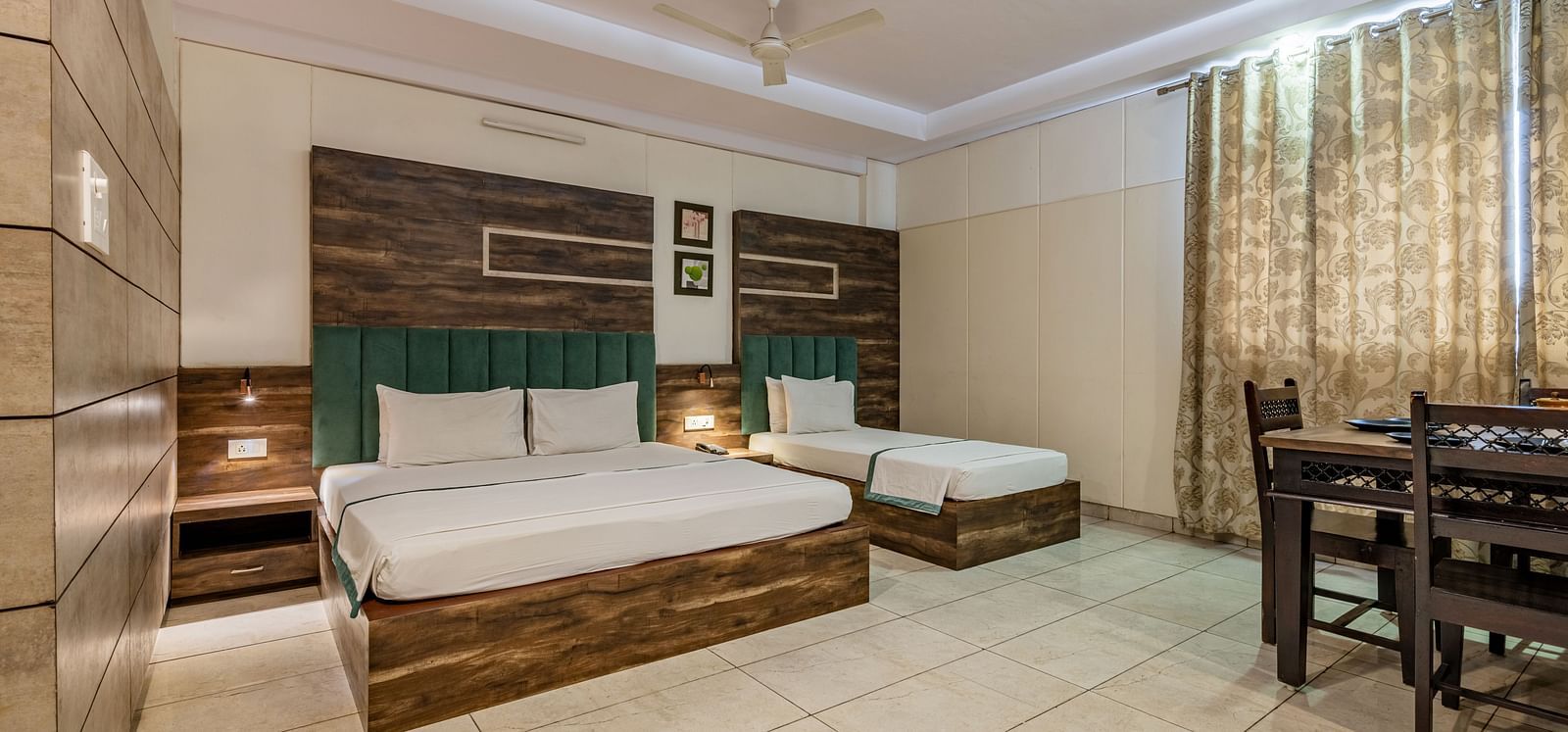 Extended view of the double and single bed, dining table and drawn curtains in the Suite of Hotel Highway King in Behror.