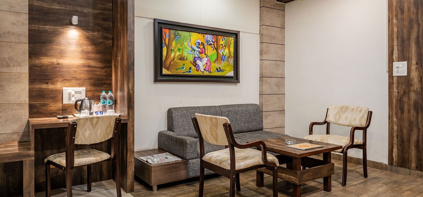Separate living area furnished with an upholstered sofa, seating chairs for two, a center table and a word desk with dedicated lighting in the Suite of Hotel Highway King in Behror.