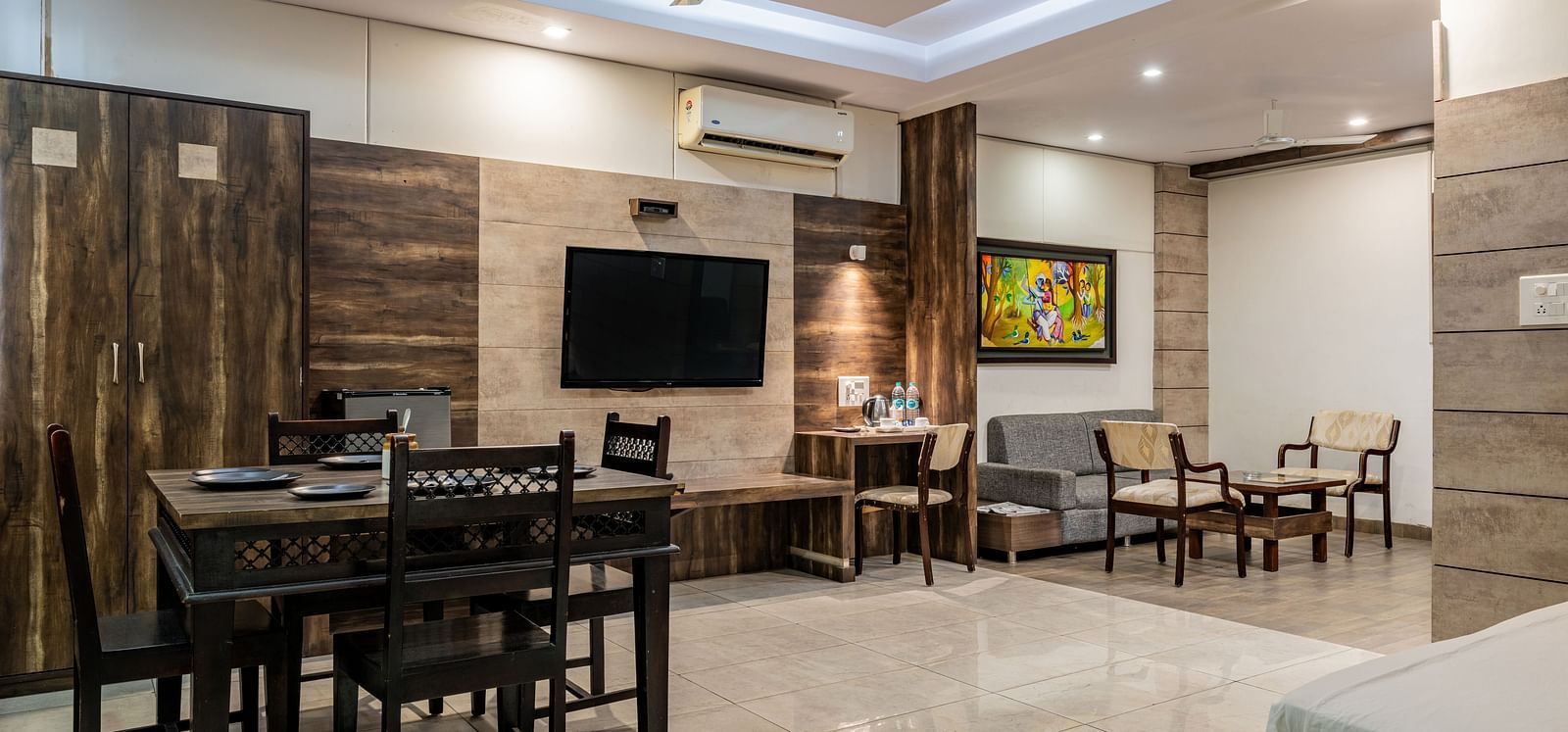 Dining table, wall-mounted TV, separate living area, and work desk in the Suite of Hotel Highway King in Behror.