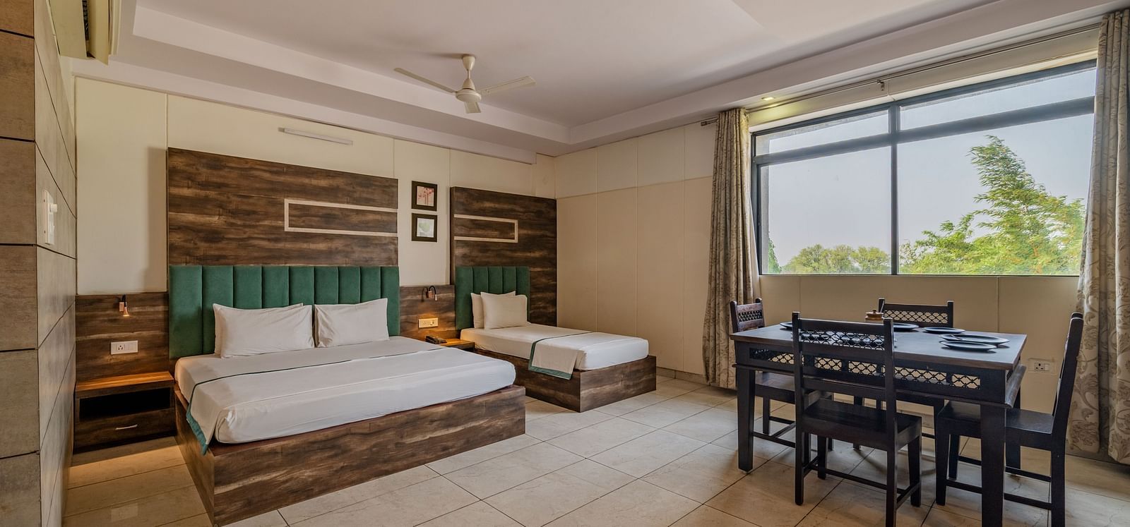 Extended view of the double and single bed, dining table and open glass windows in the Suite of Hotel Highway King in Behror.