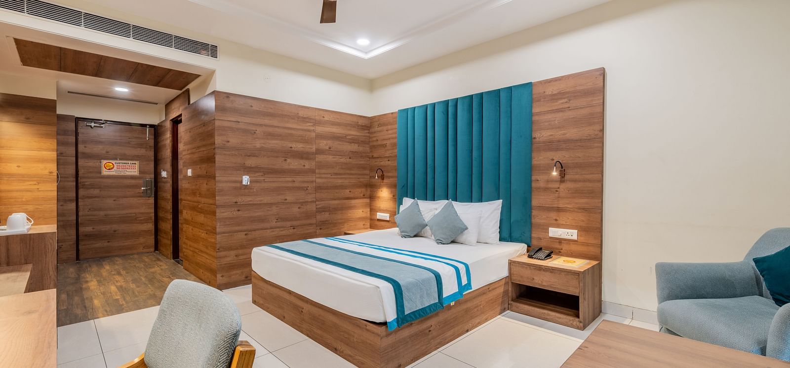 King size bed room with warm wooden tones, teal accents, and relaxed seating with a work station at Hotel Highway King, Bilaspur.