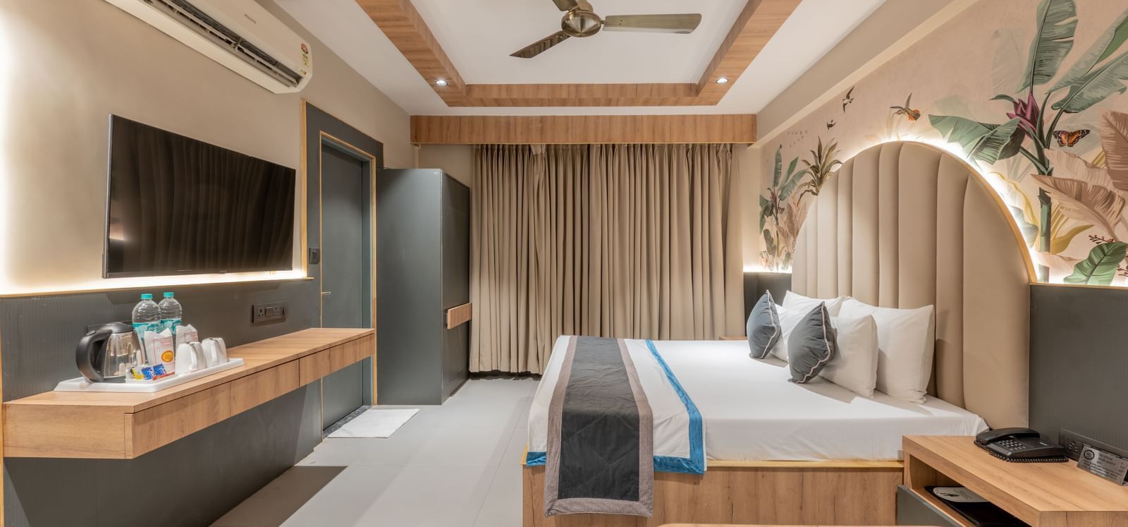 A wide view of the room featuring a king size bed, curtains, TV unit, mirror, and a wall mural at Hotel Highway King, Jaipur.