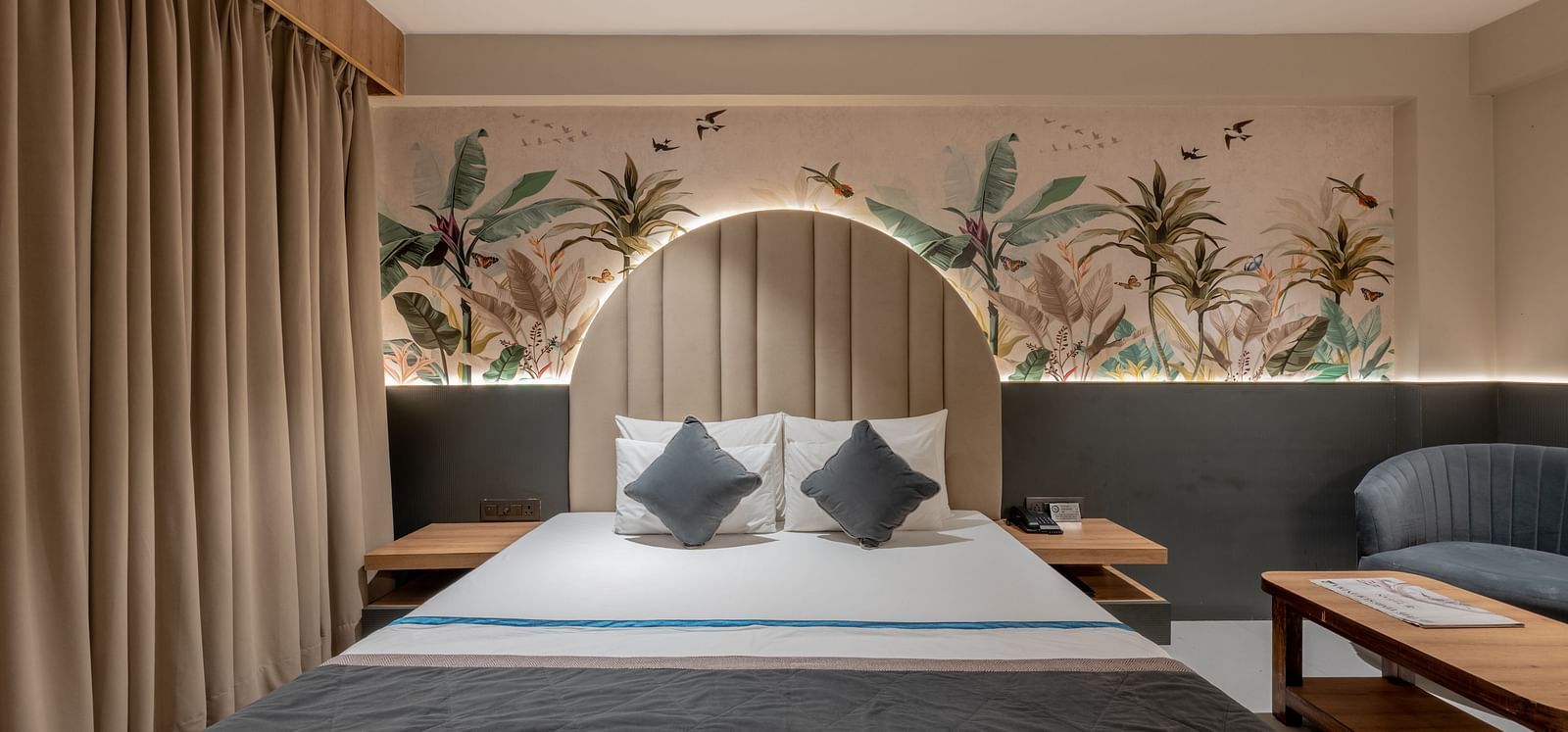 A straight-on view of a king size bed with arched headboard, nightstands and mural on the wall at Hotel Highway King, Jaipur.