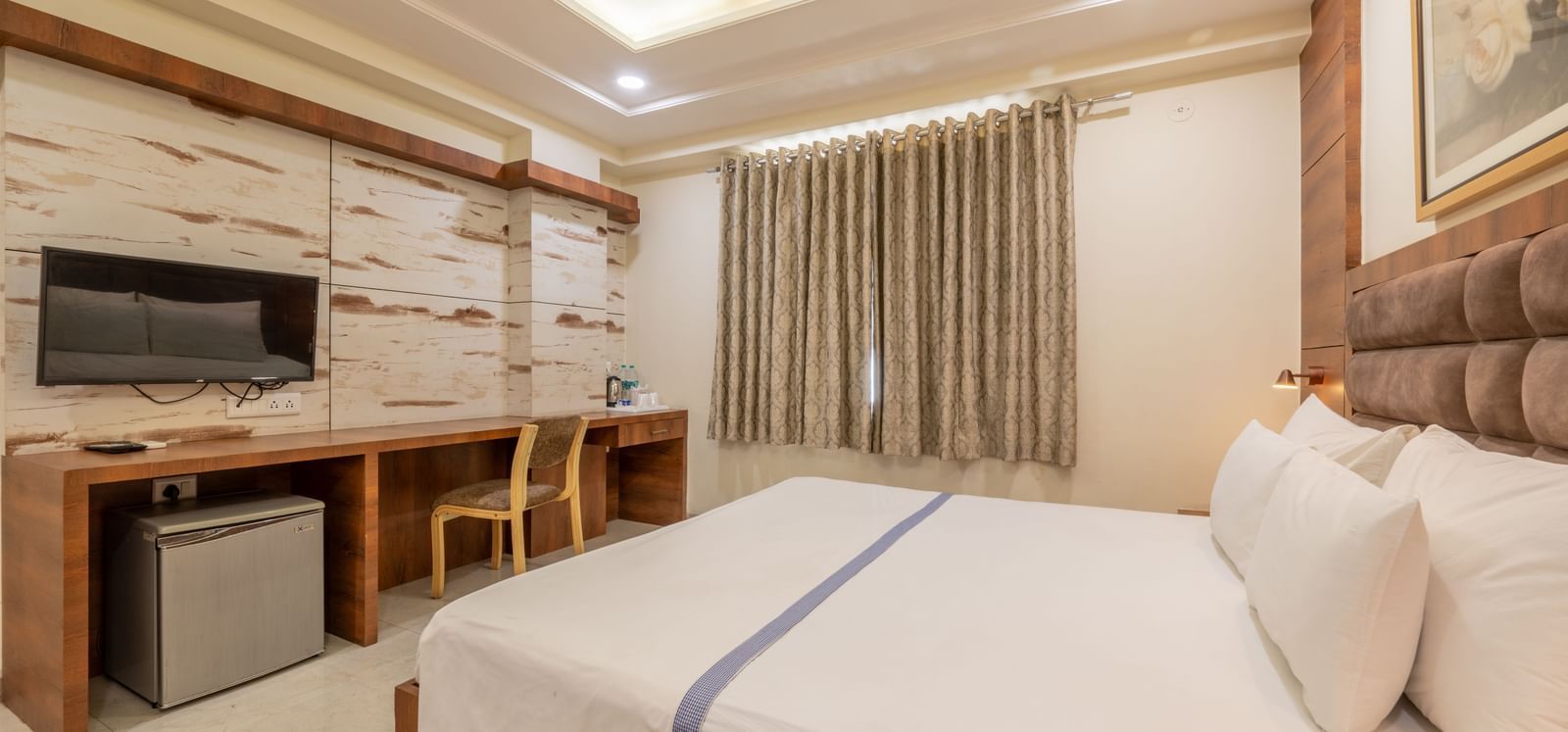 A side view of a room, featuring a king size bed, a functional work desk, and a wall-mounted television at Hotel Highway King, Jaipur.