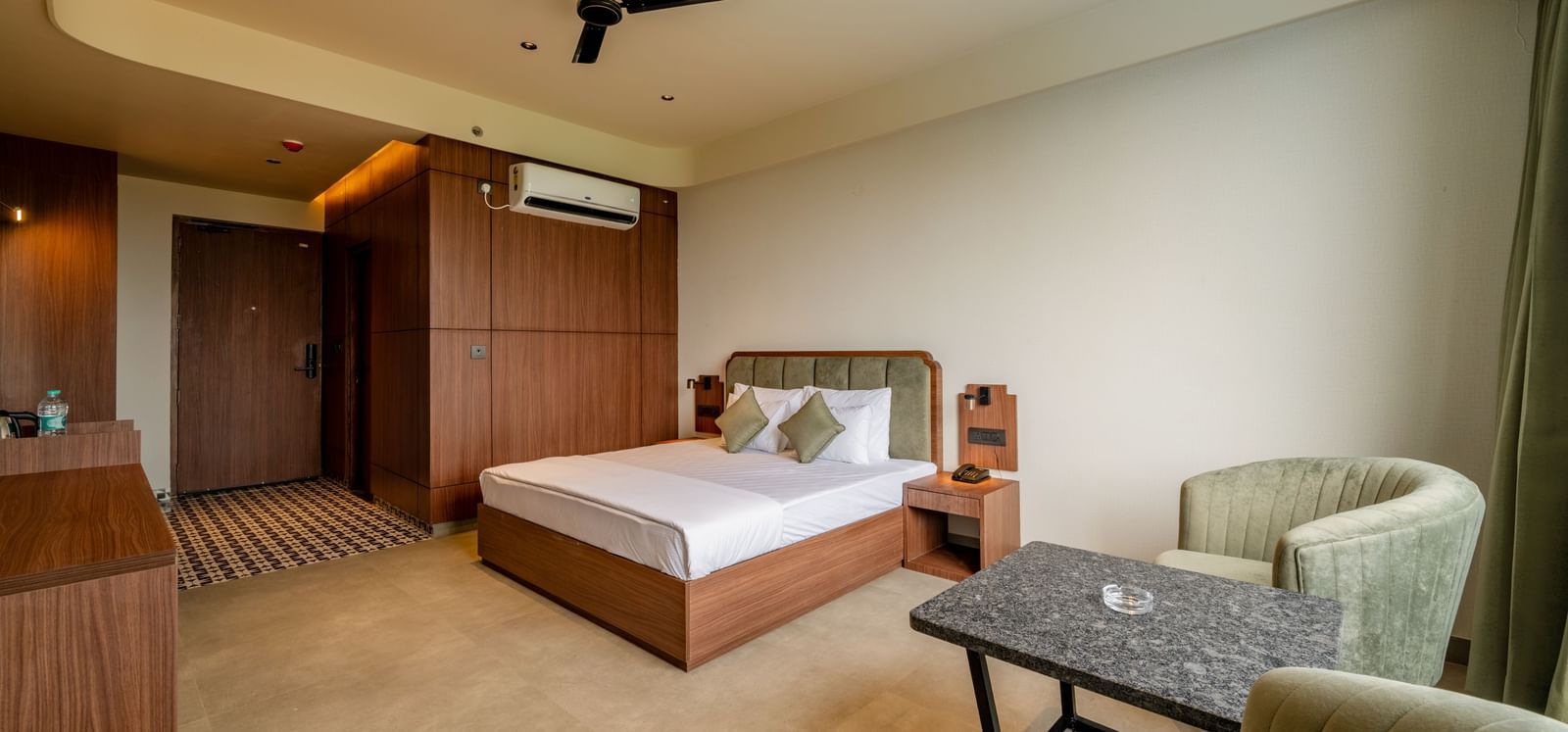 Elegant room with a large bed, armchairs, warm lighting, and a ceiling fan at Hotel Highway King, Neemrana.