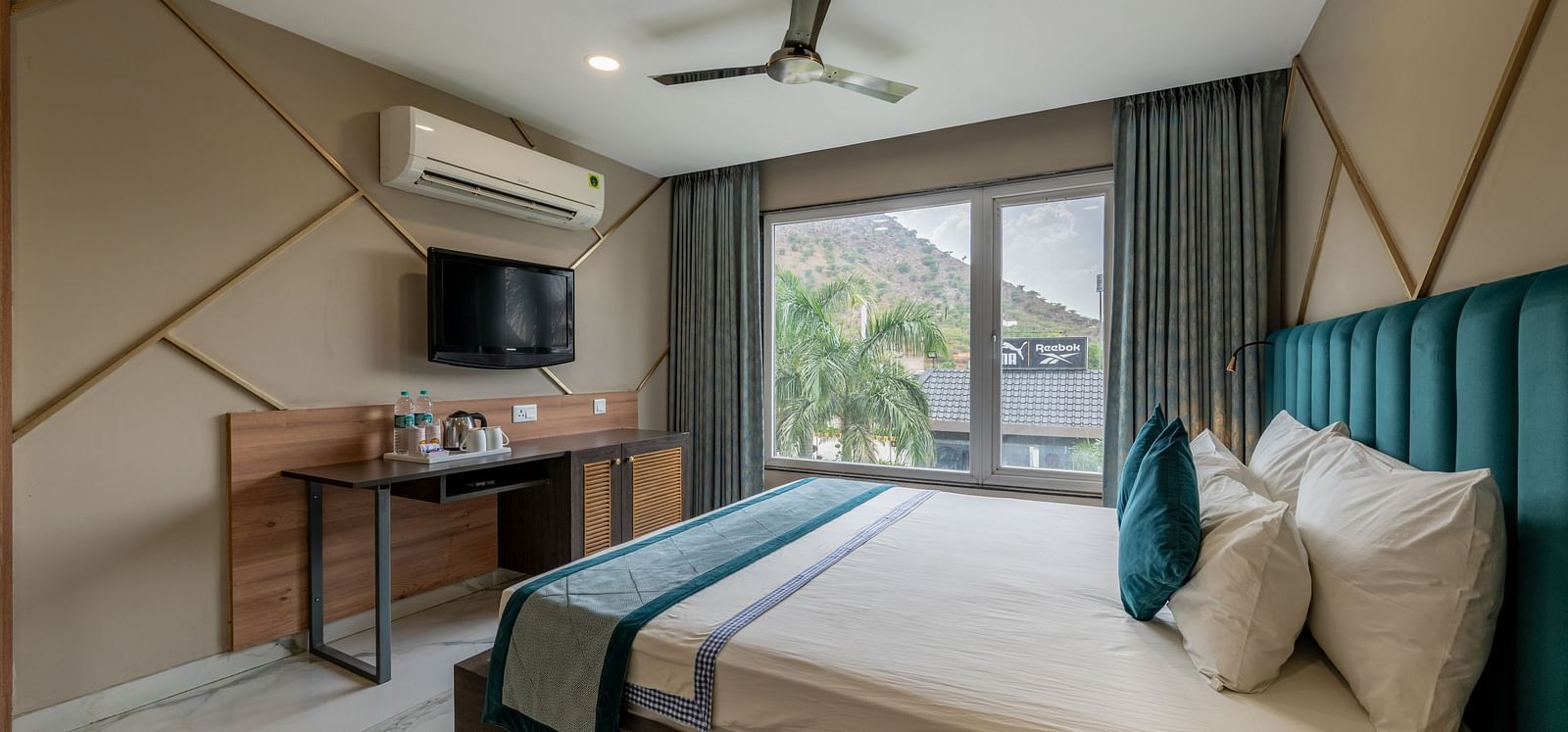 A spacious guest room with a large bed, TV, and outdoor view at Hotel Highway King Shahpura.