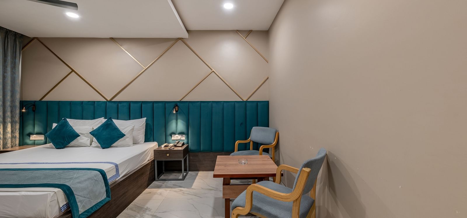 A wide shot of a comfortable guest room with a bed and a small table with chairs at Hotel Highway King Shahpura.