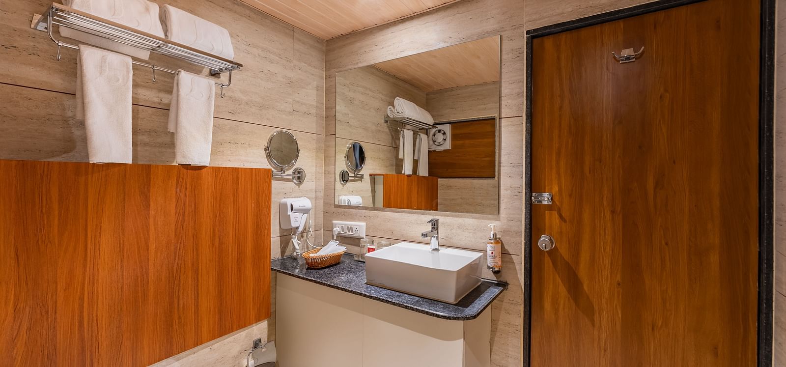 A compact bathroom features a rectangular sink on a dark countertop, a toilet, and a wooden door - Lords Eco Inn Ambaji.