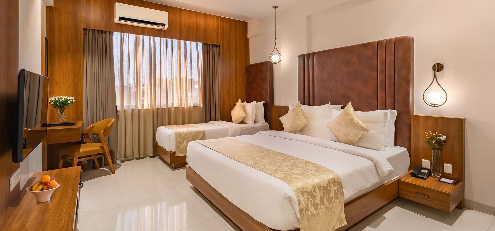 A hotel room features a comfortable king-size bed and a smaller single bed, along with a desk and a mounted television - Lords Eco Inn Ambaji.