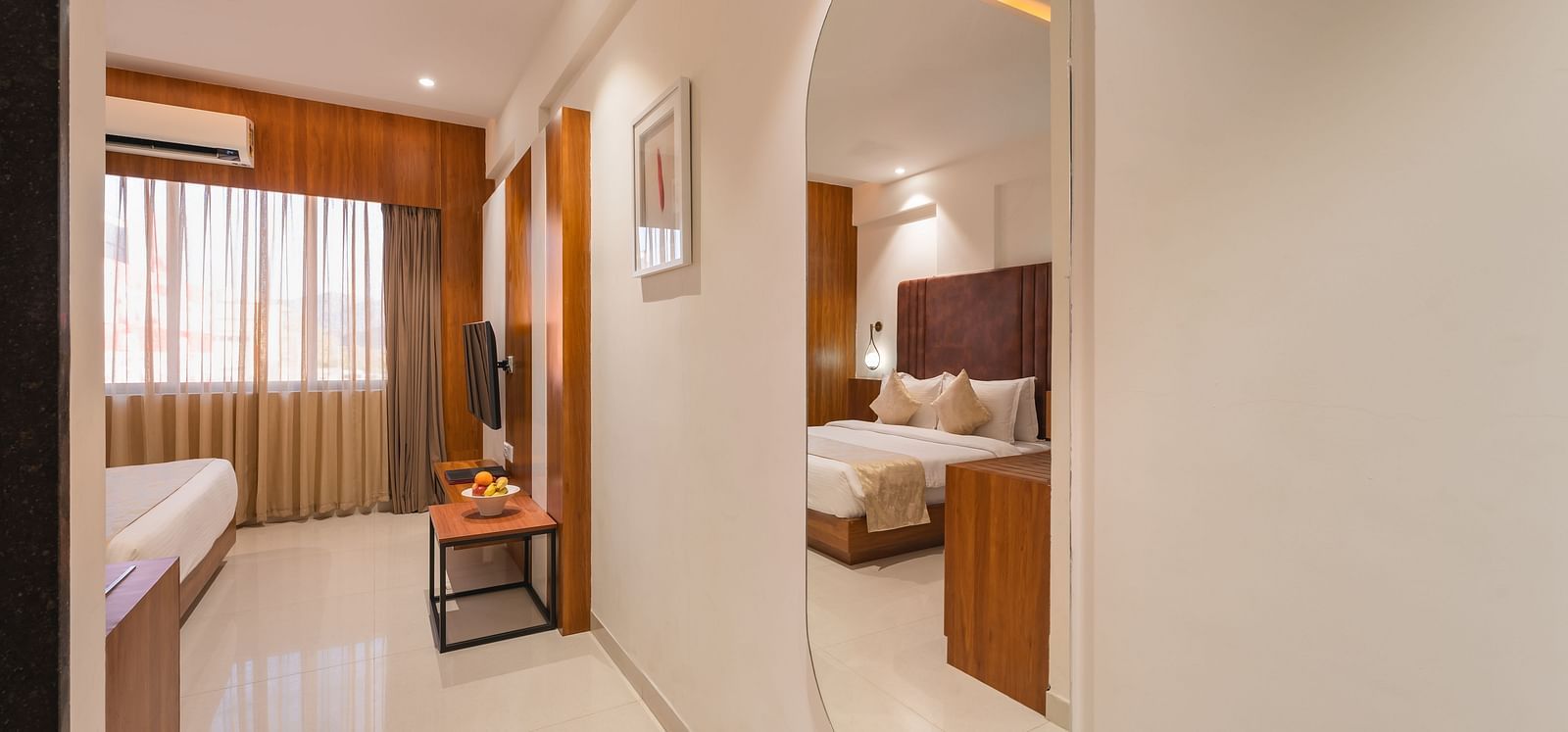 A glimpse into a hotel suite reveals a living area with a sofa and a table, leading to a bedroom with a comfortable bed - Lords Eco Inn Ambaji. 