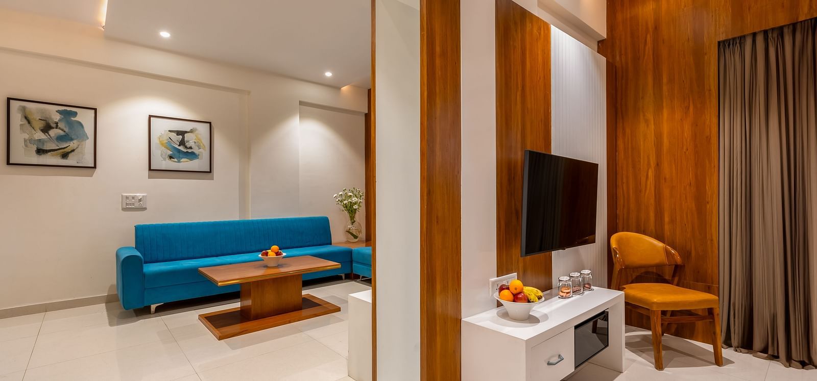 A hotel living area includes a sofa, a wooden coffee table, a mounted television, and a cushioned chair - Lords Eco Inn Ambaji.