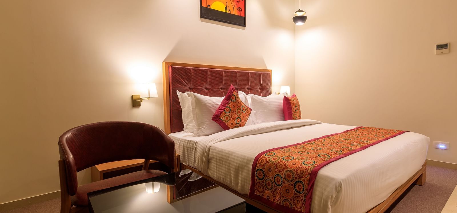 A warmly lit hotel room at Lords Eco Inn Apple Gate features a double bed with patterned accents, a chair and a small table.