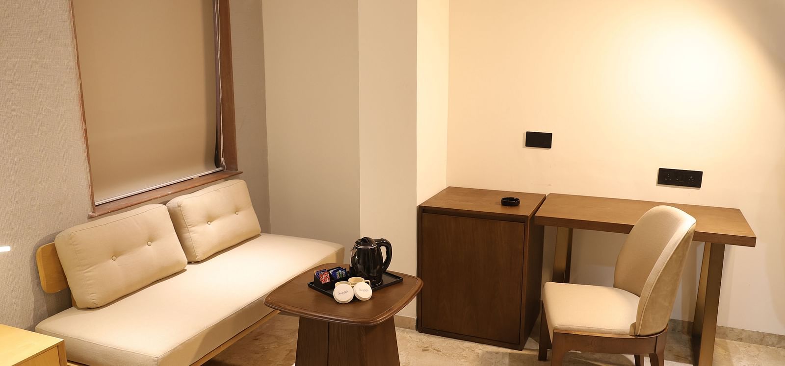 A well lit Deluxe Room at Lords Eco inn Jamnagar Maheshwari Nagar featuring a sofa bed writing desk and coffee table.