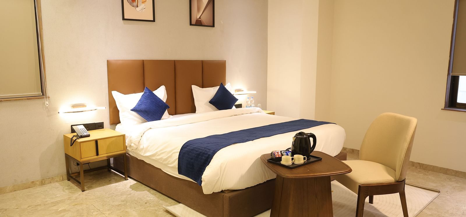 A spacious Deluxe Room at Lords Eco inn Jamnagar Maheshwari Nagar with a large bed two bedside tables and modern artwork.
