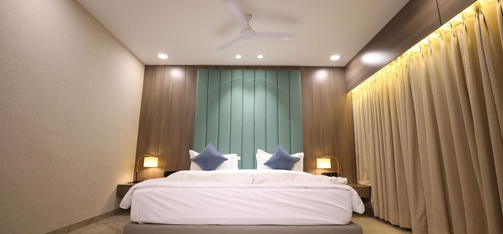 The image shows a tranquil hotel bedroom with a comfortable bed, soft pillows, gentle lighting from bedside lamps, and elegant drapery - Lords Eco Inn Navsari.