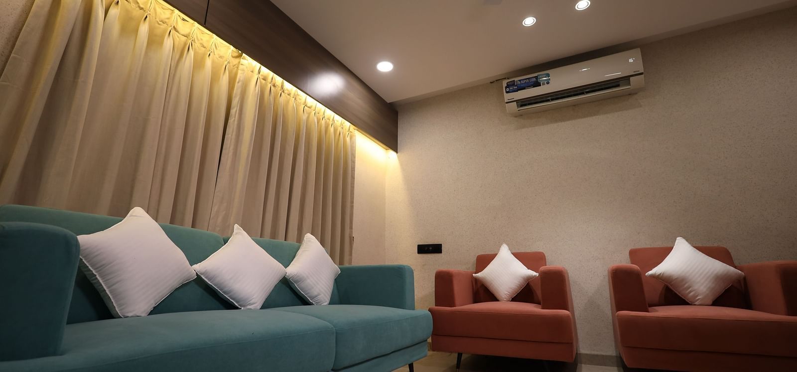 The image shows a living space with a sofa adorned with cushions and two armchairs - Lords Eco Inn Navsari.