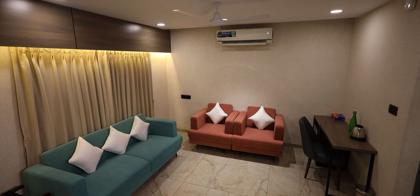 The image shows a hotel room with two sofas with cushions, a small table with chairs and amenities, and window curtains - Lords Eco Inn Navsari.