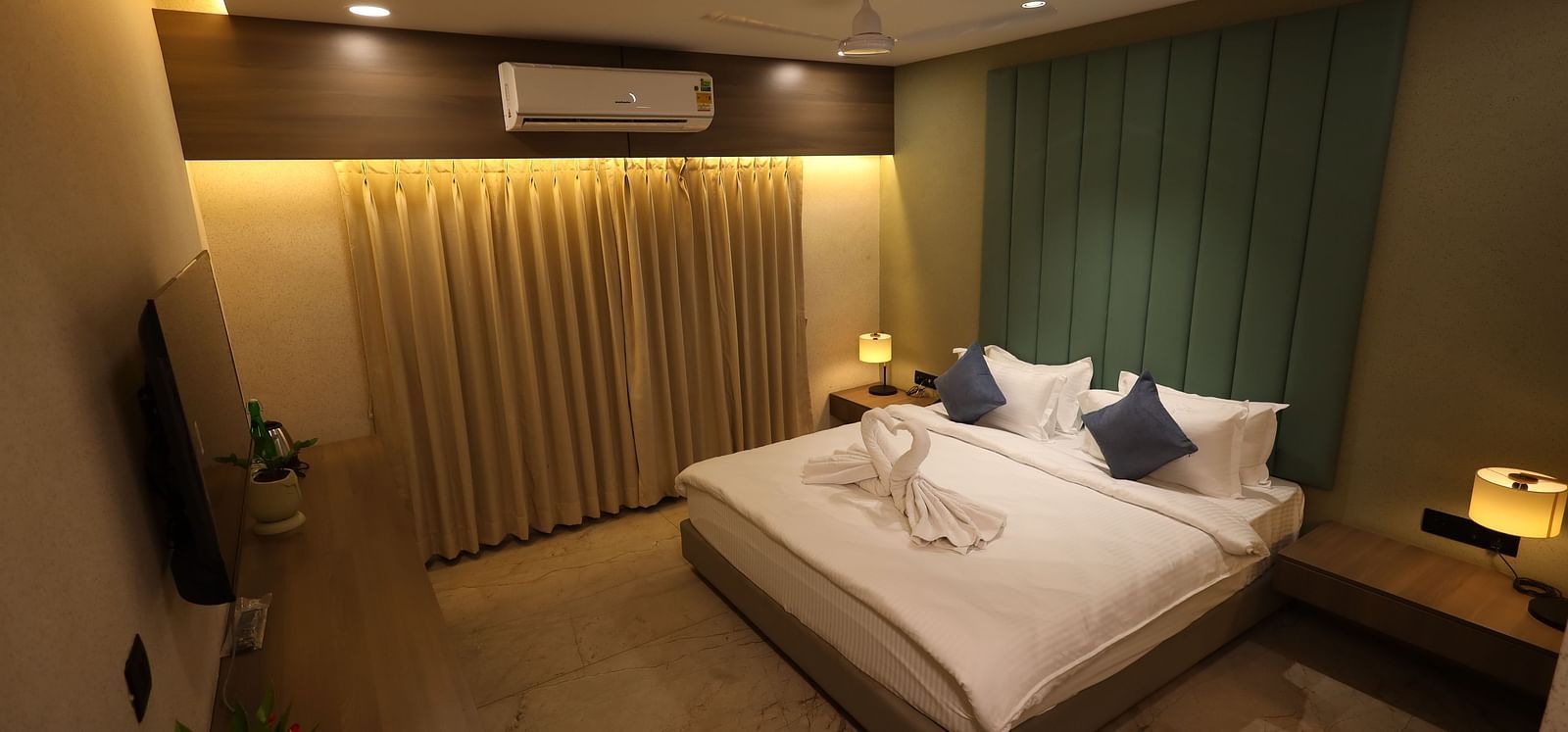 A hotel room in Bengaluru features a bed with decorative towels, nightstands with lamps, and curtains - Lords Eco Inn Navsari.