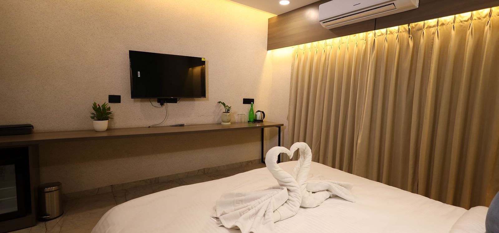 A hotel room in Bengaluru features a bed with decorative swan towels, a television, and curtains - Lords Eco Inn Navsari.