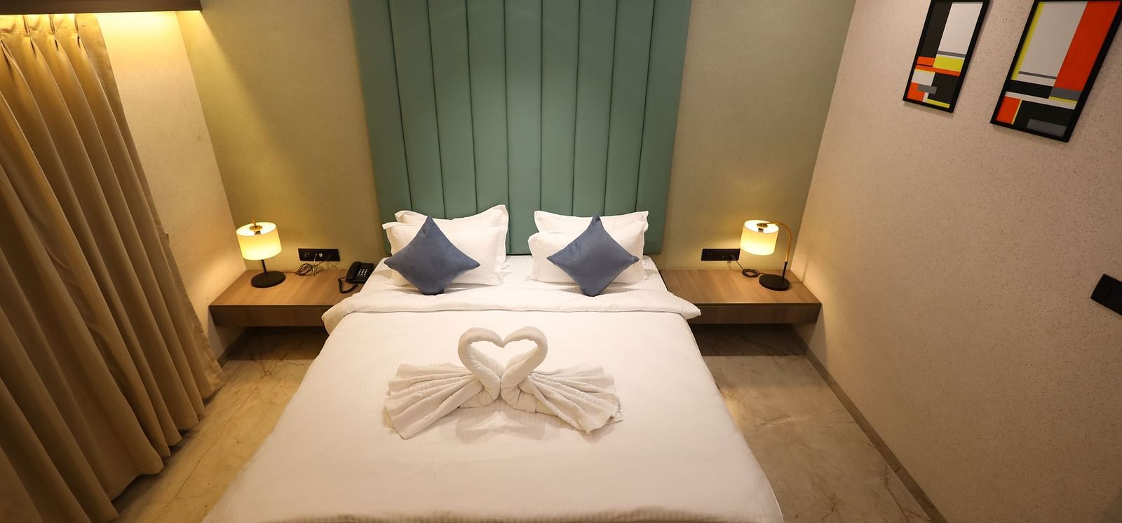 A hotel room in Navsari presents a bed with swan-shaped folded towels, flanked by nightstands and lamps - Lords Eco Inn Navsari.