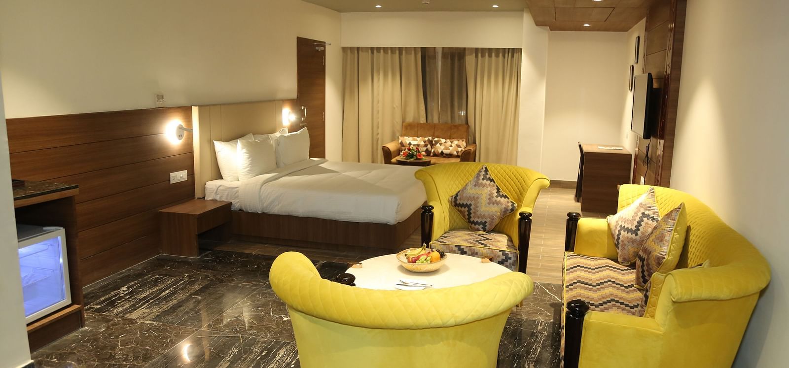 A hotel room at Lords Inn Udaipur showcases a bed, bright yellow armchairs around a small table, and modern interiors.