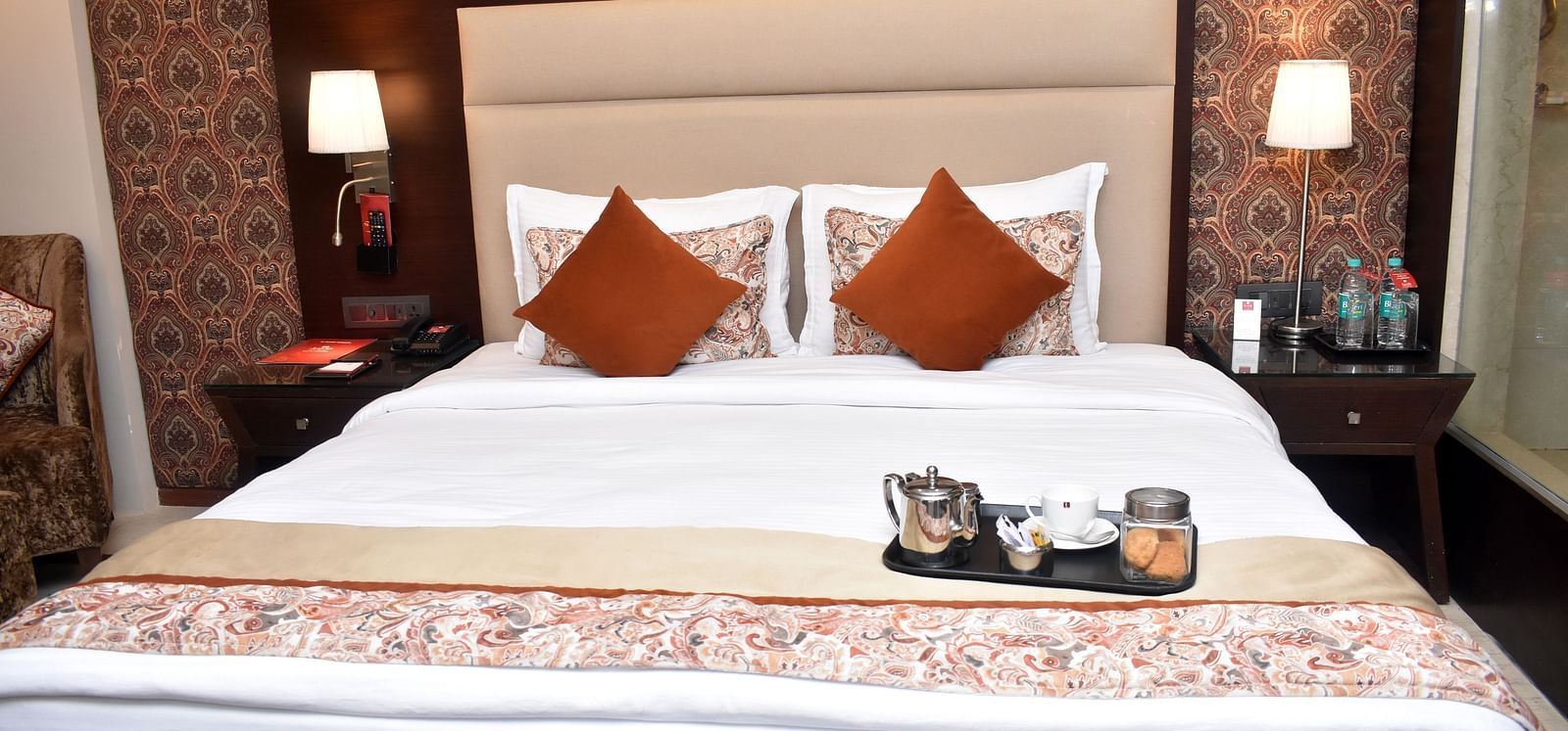 A neatly made bed with decorative pillows and a tray is in a room at Lords Plaza Surat.