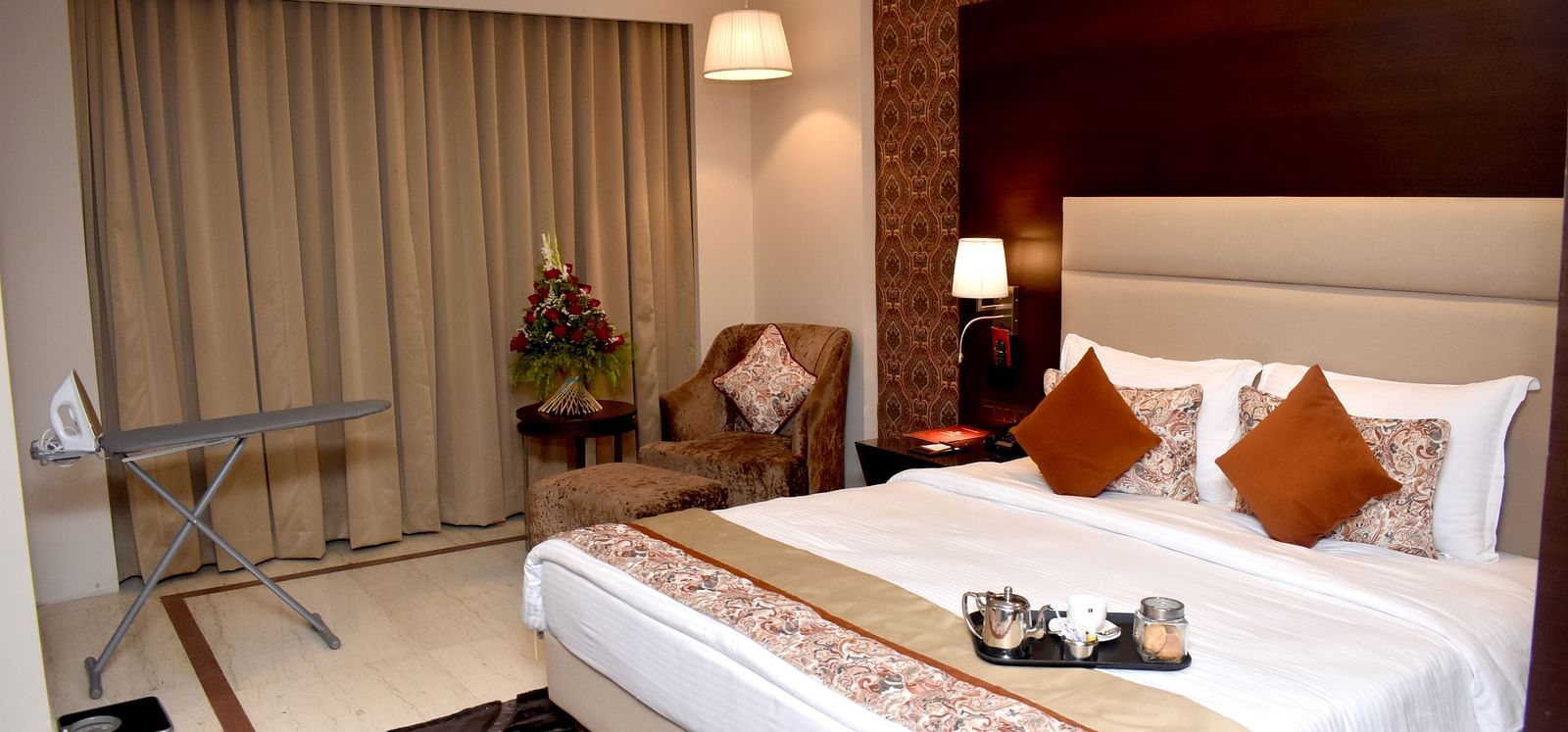 A well-lit hotel room includes a bed, seating, and window coverings at Lords Plaza Surat.