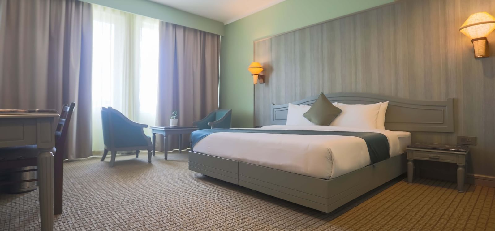 A spacious guest room at Shilton International, Kochi with a large bed, seating area, and desk.