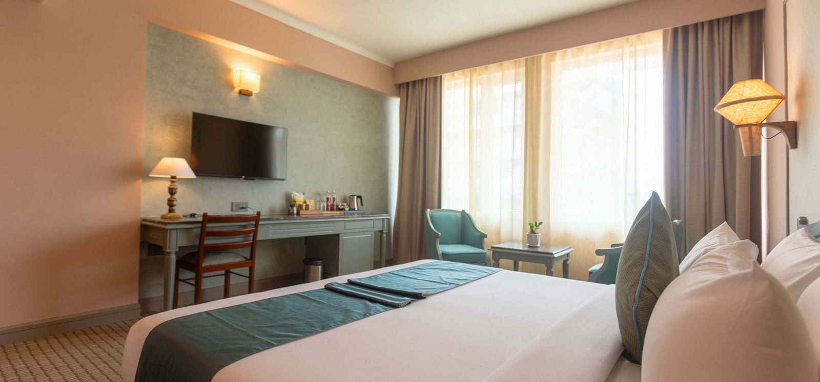 A guest room at Shilton International, Kochi with a large bed, a desk area, and a window.
