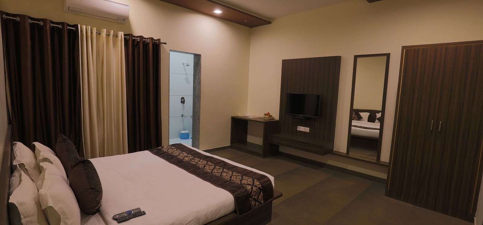 A comfortable bedroom with a double bed, dark furniture, and soft lighting - Vishal Lords Inn Gir Forest
