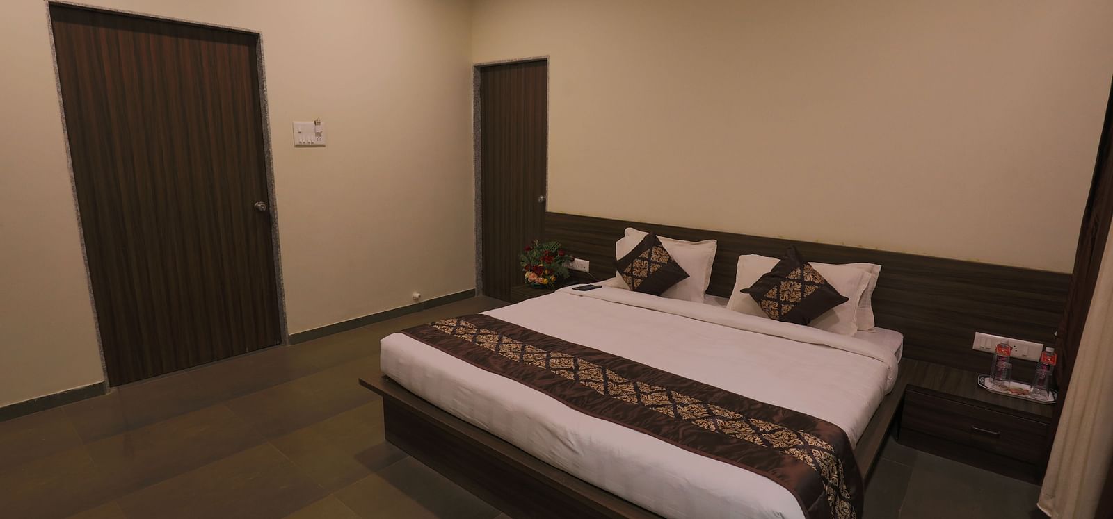 A bedroom with a double bed, dark wooden furniture, and a closed door - Vishal Lords Inn Gir Forest