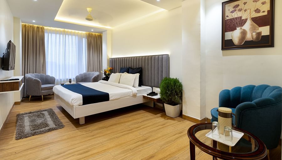 A room featuring a wall painting, a bed, a TV, sofa chairs and a table - Hotel Meghdoot, Bhopal