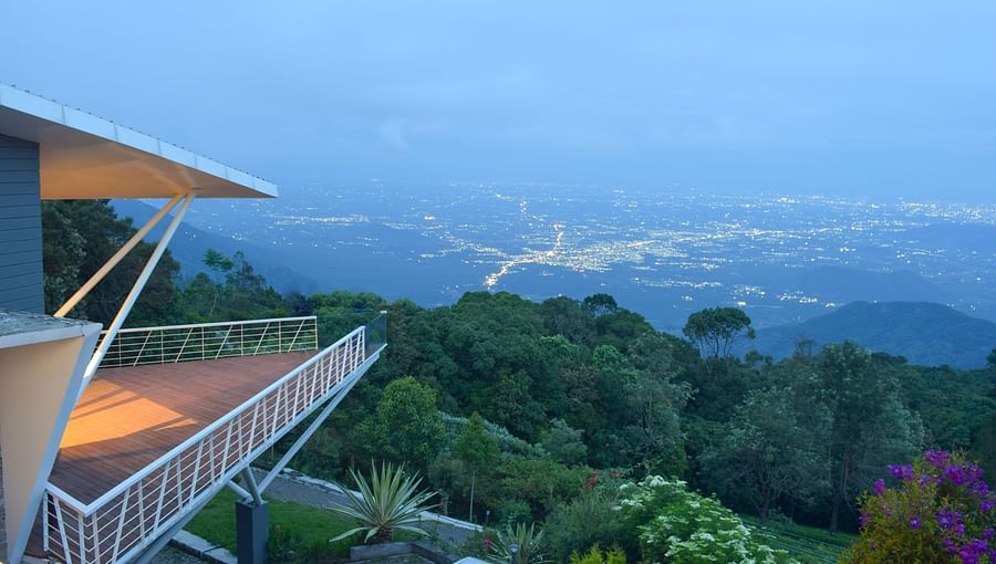 Twilight view of a balcony overlooking a lush valley and distant mountains at Ibex Resorts, Coonoor (Tapas).