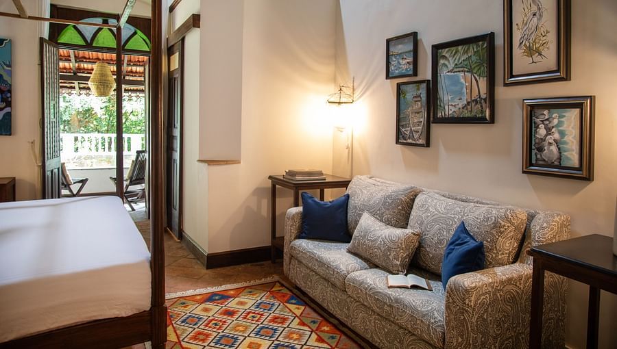 An image of a beautiful grand bedroom  with seating area, photo frames hanging on the wall and there is also a table with lamp - Lamrin Ucassaim Hotel, Goa