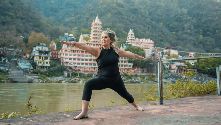 A woman practising the Warrior II yoga pose on a terrace overlooking the River and mountains.